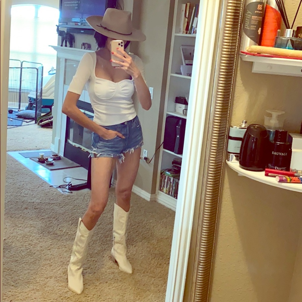 White top, denim ripped shorts, cowboy boots & hat